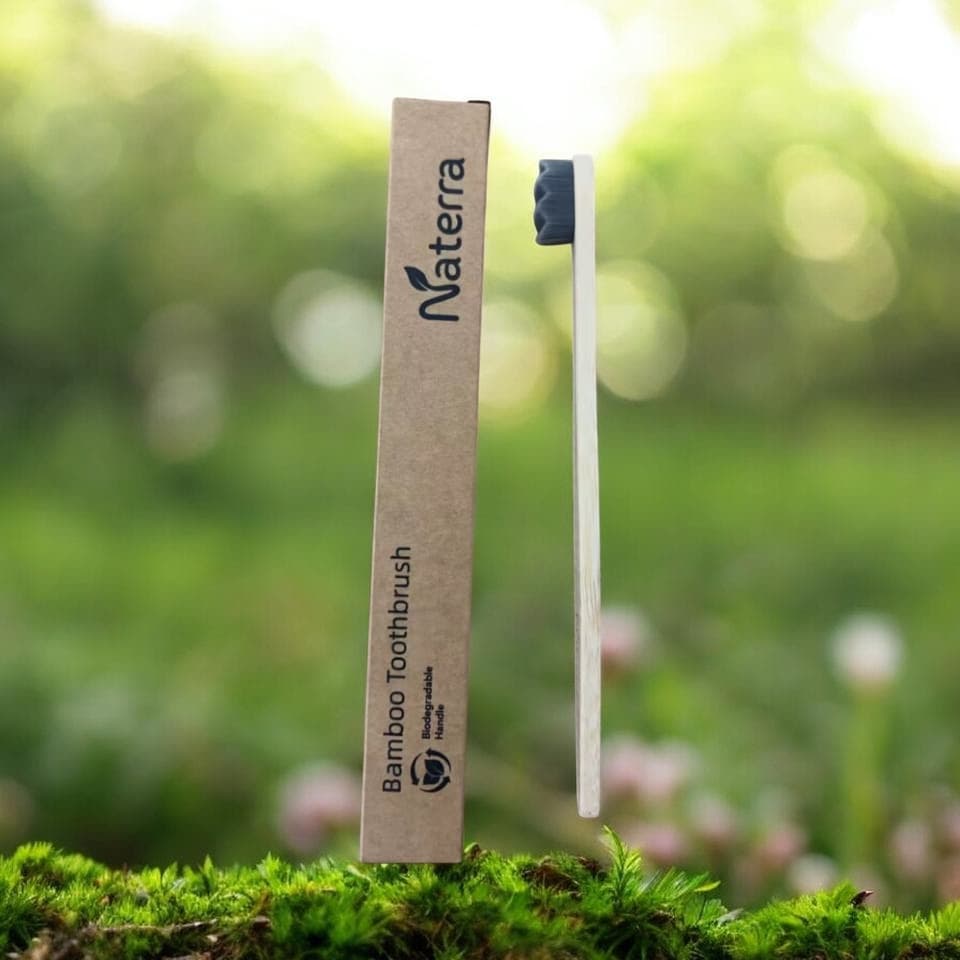 Naterra Bamboo Toothbrush with black bristles, standing upright on moss